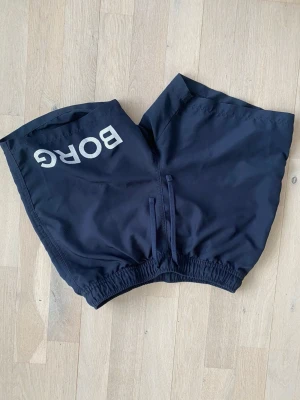 Svarta badshorts från Björn Borg - Snygga blåa badshorts från Björn Borg med resår i midjan och snörning framtill. Stora vita Borg-trycket på ena benet, perfekt nu till sommaren ☀️