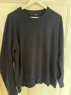 Svart sweatshirt från 157, storlek M - En basic svart sweatshirt från 157 i storlek M. Tröjan har rund halsringning, ribbade muddar vid ärmslut och nederkant. Perfekt för en chill och avslappnad stil. Materialet känns mjukt och bekvämt mot huden.