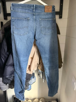 Ljusblå slim fit jeans från Jack & Jones - Säljer ett par ljusblå slim fit jeans från Nudie med klassisk femficksdesign och diskreta slitningar framtill. Jeansen har raka ben och är tillverkade i mjuk denim med en snygg tvättad look. Perfekta för en avslappnad och trendig stil.