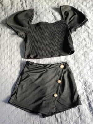Svart set från Emery Rose XS - Toppen har ribbad struktur och puffärmar, medan kjolen har omlott-look med tre dekorativa guldknappar. Perfekt för dig som gillar trendiga detaljer och en stilren look kjolen är i xs och toppen i L💗