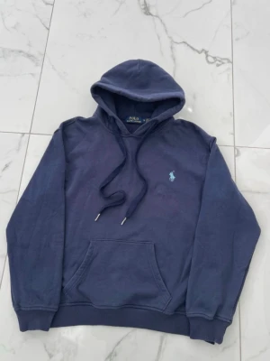 Äkta hoodie från Polo Ralph Lauren - Snygg mörkblå hoodie från Polo Ralph Lauren med klassisk huva och dragsko. Har en broderad logga i ljusblått på bröstet och en stor magficka. Perfekt för en chill och stilren look.