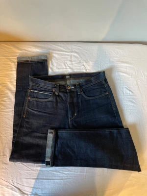 Mörkblå selvedge jeans - Säljer ett par mörkblå jeans med klassisk femficksdesign och kontrastsömmar. Jeansen har raka ben och är tillverkade i kraftig denim. Perfekta för dig som gillar en stilren och tidlös look.