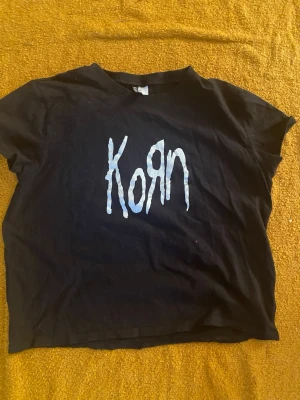 Svart Korn t-shirt med tryck - Cool svart t-shirt med Korn-logga i vitt på bröstet. Klassisk passform med korta ärmar och rund hals. Perfekt för dig som gillar bandmerch och vill ha en edgy stil.