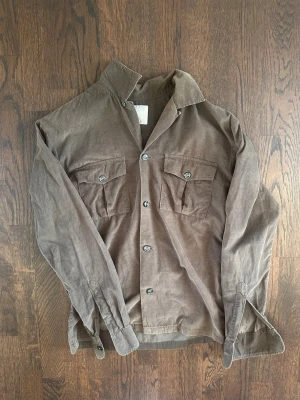 Oscar Jacobson Henrik Reg Shirt Wash Men Small Green - Oscar Jacobson Henrik Regular Fit-skjorta i mörkgrönt. Tillverkad i lätt, tvättat linne för en mjuk och avslappnad känsla samt mycket hög komfort. Har klassisk krage, genomgående knäppning framtill och två bröstfickor med knappar för en stilren, utility-inspirerad look.  Högra ärmen är något missfärgad, men inget man direkt tänker på – snarare ger det en lite cool karaktär. Nypris: 1500-1700 SEK Pris : 500 SEK