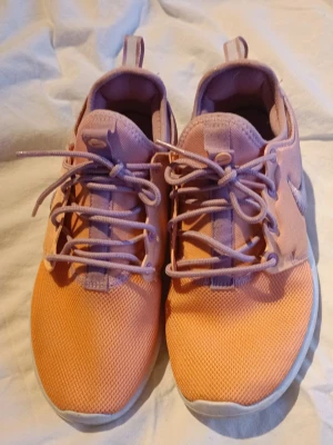 Nike Roshe  - Säljer ett par Nike Roshe One sneakers i snyggt rosa , orange och lila meshmaterial med silvrig swoosh på sidan. Skorna har lågt skaft, vita sulor och matchande lila skosnören. Perfekta för dig som vill ha en färgglad och sportig look.