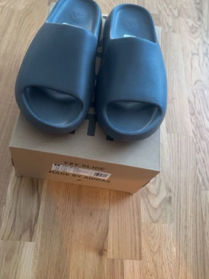 Adidas Yeezy Slide Slate Grey - Yeezy slides slate grey storlek us 11. Obs! De är små i storleken och passar us 10 alltså 44. De är helt oanvända och i perfekt skick. Orderbekräftelse finns och kan visas vid förfrågan, samma gäller fler bilder på varan. Ett par sköna slides perfekt nu till sommaren.