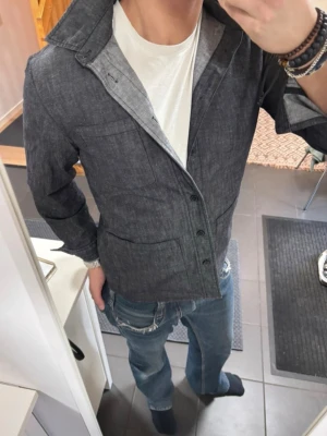 Mörkgrå overshirt  - Snygg mörkgrå overshirt med klassisk krage och knäppning framtill. Overshirten är från east west och i storlek M, passar dig som är 175-185.
