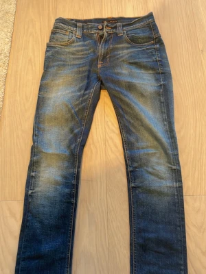 Nudie Jeans  - Säljer ett par blå jeans från Nudie Jeans med klassiska orange sömmar och broderad bakficka. Jeansen har en tvättad look och raka ben. Perfekta för dig som gillar en avslappnad men ändå stilren stil. Inga tecken på användning. Sjukt bra passform! Hör av er vid minsta fundering!