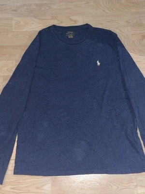 Mörkblå långärmad topp från Polo Ralph Lauren - Mörkblå långärmad topp från Polo Ralph Lauren med klassisk rund hals och ikonisk broderad logga på bröstet. Tillverkad i mjuk bomull som känns skön mot huden. Perfekt för en chill och stilren look.