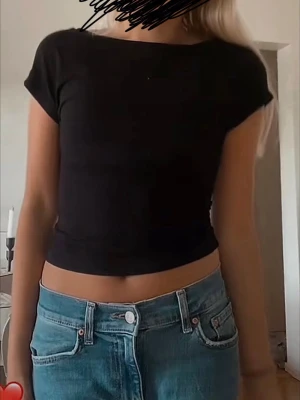 Svart topp med öppen rygg - En enkel svart topp med korta ärmar och rund halsringning. T-shirten har öppen rygg och passar perfekt inför sommaren. Den är i stolek XS. 
