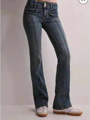 Blå bootcut jeans med fickdetaljer - Säljer ett par blå lågmidjade bootcut jeans med unika fickor framtill. Använda men i  bra skick! Köpta för 700. Slitna längst ner, skriv för bilder!