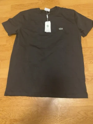 Svart t-shirt från Lacoste - Klassisk svart t-shirt från Lacoste med den ikoniska krokodilloggan broderad på bröstet. T-shirten har rund halsringning och korta ärmar, perfekt för en stilren och enkel look.