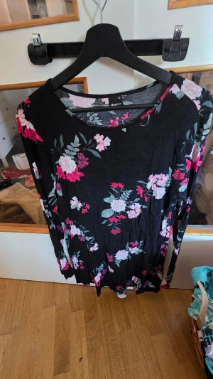 Blommig svart klänning Gina Tricot - Svart klänning från Gina Tricot med blommigt mönster i rosa, vitt och grönt. Långärmad modell med rund halsringning och mjukt, stretchigt material. Perfekt för dig som gillar en feminin och bekväm stil.