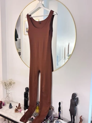 Brun  jumpsuit i stretch - Snygg brun jumpsuit med tight passform och rund halsringning. Tillverkad i ett stretchigt material som sitter skönt mot kroppen. Perfekt för en trendig och avslappnad look.