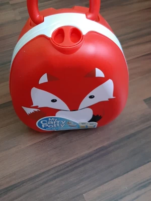 Helt ny. Röd My Carry Potty med rävmotiv - Helt ny, aldrig används. Passar för resan. Säljer en bärbar potta från My Carry Potty i röd plast med ett gulligt rävansikte på framsidan. Praktisk att ta med tack vare handtaget och smidig design. Perfekt för småbarn som håller på att potträna.