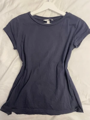 Mörkblå t-shirt från H&M - En enkel och stilren mörkblå t-shirt från H&M. Modellen är figurnära med rund halsringning och korta ärmar. Tillverkad i mjuk bomull som känns skön mot huden. Perfekt för en avslappnad och snygg look.