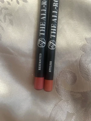 W7 The All-Rounder Läppennor 2-pack Restricted / Stylish - Två läppennor från W7 i nyanserna Restricted (mauve-rosa) och Stylish (varm nude). Pennorna har matt finish och klassisk pennform med svart hylsa och färgmarkerad ände. Perfekta för att definiera och fylla i läpparna med precision. Båda är använda men Stylish endast testad.