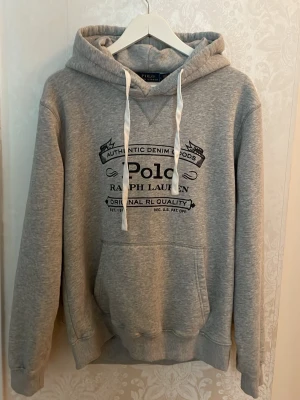 Grå hoodie från Polo Ralph Lauren - Tvär skön grå hoodie från Polo Ralph Lauren med fet design frampå. Hoodien är i Storlek L och är i princip nytt skick! Vid funderingar och intresse kom dm! 🔥🥂