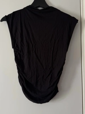 Svart ärmlös topp i bomull från Gina Tricot - En svart, enkel och stilren ärmlös topp i mjuk bomull från Gina Tricot. Modellen har en tajt passform och rund halsringning, perfekt att matcha med jeans eller kjol. Snyggt basic-plagg för en clean look.