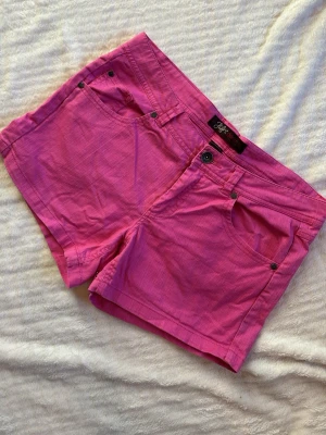Rosa jeansshorts - Snygga rosa shorts från Ellos med låg midja. Modellen är kort och har bälteshällor samt svarta nitar vid fickorna. Midjemått rakt över: ca 42 cm