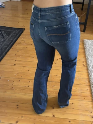 Blå lee bootcut jeans med låg midja - Säljer ett par blå lee bootcut jeans med låg midja. Jeansen har snygga slitningar och kontrastsömmar. Står ingen storlek men jag som har s/m tycker dom sitter lite tajt