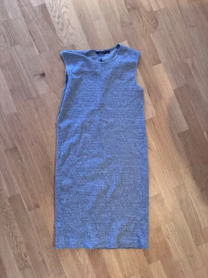 Grå ärmlös ribbad klänning - En stilren grå ärmlös klänning i ribbat material. Klänningen har en rak passform och rund halsringning, perfekt för en enkel och avslappnad look.