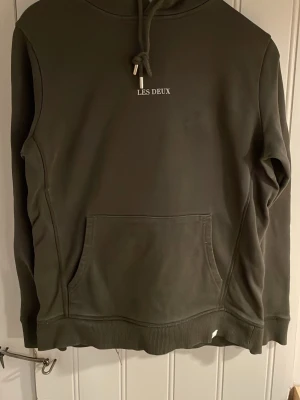 Mörkgrön hoodie från Les Deux - Snygg mörkgrön hoodie från Les Deux med broderad logga på bröstet. Klassisk känguruficka framtill, ribbade muddar och justerbar huva med snören. Perfekt för en avslappnad och stilren look.