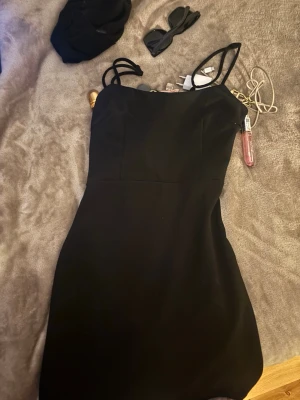 Svart kort klänning med tunna band - Säljer en svart kort klänning med tunna axelband och enkel, stilren design. Klänningen har en omlottliknande detalj framtill och är figurnära i modellen. Perfekt för dig som gillar minimalistisk och trendig stil.