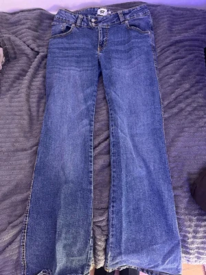 Blå bootcut jeans från 157 - Säljer ett par klassiska blå bootcut jeans från 157 med kontrastsömmar och femficksmodell. Jeansen har normal midja och stängs med två knappar och dragkedja. Tillverkade i slitstark denim som ger en tidlös look.