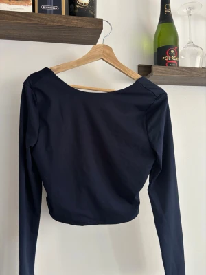 Svart croppad långärmad topp - Snygg svart croppad topp med lång ärm och djup, fyrkantig urringning. Perfekt att styla med höga jeans eller kjol. Tunn och stretchig i materialet för en bekväm passform.