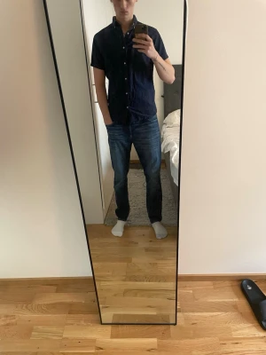 Mörkblå kortärmad skjorta - Säljer en stilren mörkblå skjorta med korta ärmar och klassisk krage. Skjortan har knappar framtill och en enkel, tidlös design som passar till det mesta. Perfekt för dig som gillar en clean och avslappnad look.