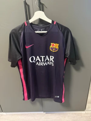 FC Barcelona Neymar Jr matchtröja - Säljer en svart och rosa FC Barcelona matchtröja från Nike med Neymar Jr och nummer 11 på ryggen. Tröjan har klubbmärke, Qatar Airways-tryck på bröstet och rosa detaljer längs sidorna. Tillverkad i lätt och ventilerande material, perfekt för fotbollsträning.