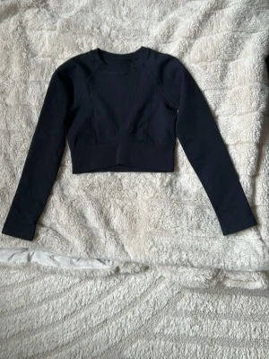Träningstopp/tröja - Snygg svart croppad topp med lång ärm och rund hals. Materialet är ribbat och stretchigt vilket ger en bekväm passform. Aldrig använd🖤(OBS!! Bilderna är lånade, samt att det inte är samma topp/märke som på bilden som jag säljer utan det är för att se hur den sitter på).