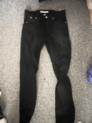 Svarta jeans från Calvin Klein - Snygga svarta jeans från Calvin Klein med klassisk femficksdesign och diskret CK-logo vid fickan. Jeansen har en smal passform och är tillverkade i ett mjukt och stretchigt material för extra komfort. Perfekta för en stilren och modern look. Säljes i befintligt skick
