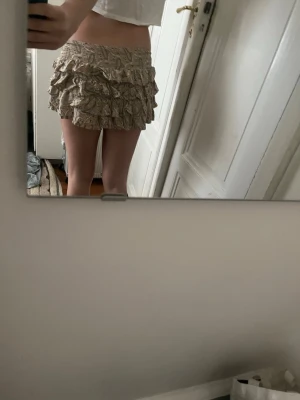 Beige volangkjol med mönster - Supersöt beige kortkjol med flera lager volanger och diskret mönster. Kjolen har en elastisk midja och är perfekt för dig som gillar en lekfull och trendig stil. Materialet känns lätt och luftigt, vilket gör den skön att bära under varmare dagar.