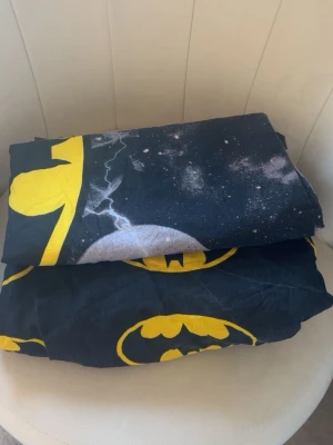 Batman påslakan och örngott svart och gult - Säljer ett coolt påslakanset och ett örngott med Batman-tryck i svart och gult. Setet har stora Batman-loggor och ett rymdinspirerat mönster med blixtar och stjärnor. Perfekt för dig som gillar superhjältar och vill ha något unikt i sovrummet.