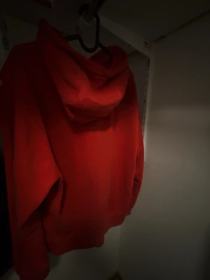 Röd Nike hoodie med huva - Snygg röd hoodie från Nike med klassisk logga på bröstet. Hoodien har en stor ficka framtill, dragsko i huvan och ribbade muddar vid ärmslut och nederkant. Perfekt för en avslappnad och sportig stil.