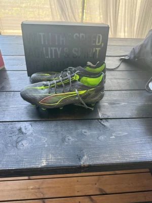 Puma gråa fotbollsskor med neon - Säljer ett par gråa Puma fotbollsskor med neonfärgade detaljer och sula. Är i bra skick!