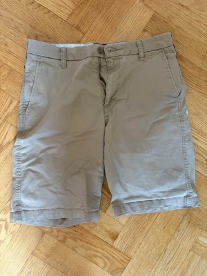 Beiga shorts med fickor - Snygga beige shorts i bomull med klassisk passform. De har bälteshällor, sidofickor och två bakfickor. Perfekta för varma dagar och enkel att matcha med olika stilar.