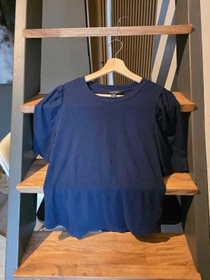 Mörkblå ribbad topp från lauren ralph lauren  - Mörkblå ribbad topp från LRL med rund halsringning och puffiga trekvartsärmar. Tidlös och enkel design som passar till mycket. Materialet känns mjukt och stretchigt.