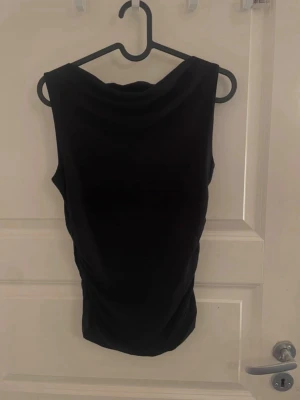 Svart ärmlös topp från BikBok - Snygg svart ärmlös topp från BikBok med draperad halsringning. Toppen har en figurnära passform och är tillverkad i ett mjukt, stretchigt material. Mycket bra skick
