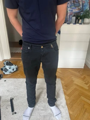Svarta slim-fit jeans från Tramarossa - Säljer ett par svarta slim-fit jeans från Tramarossa med klassisk femficksdesign och guldfärgad knapp. Jeansen har en modern passform som sitter snyggt längs benen och är tillverkade i bomull med lite stretch för extra komfort.