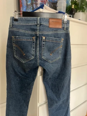 Blå jeans från Dondup - Snygga blå jeans från Dondup med klassisk femficksdesign och läderpatch bak. Jeansen har raka ben och kontrastsömmar, tillverkade i slitstark denim. Perfekta för dig som vill ha ett stilrent och tidlöst plagg i garderoben.