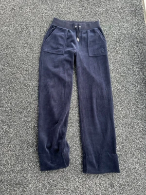 Mörkblå velour mjukisbyxor Juicy Couture - Mörkblå mjukisbyxor i velour från Juicy Couture med bred resårmidja och dragsko. Byxorna har stora fickor fram och bak, samt raka ben med breda benslut. Perfekta för en chill och avslappnad stil. Alla detaljer kvar. Nypris 1200 kr