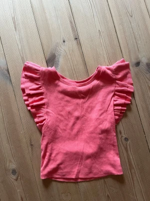 Rosa croppad topp med volangärmar - Söt rosa croppad topp med ribbad struktur och volangdetaljer på ärmarna. Perfekt för dig som vill ha en trendig och lekfull look. Toppen har rund halsringning och är tillverkad i mjukt material som känns skönt mot huden.