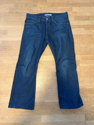 Levi's 512 Bootcut Jeans blå - Säljer ett par klassiska Levi's 512 bootcut jeans i mörkblå denim. Jeansen har fem fickor, normal midja och utsvängda ben. Perfekta för dig som gillar en tidlös och avslappnad stil. Materialet är slitstark bomullsdenim. Archive Waist:44cm Längd: 100cm