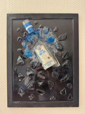 Tavla med ginflaska och glaseffekt - Tillverkad av mig själv. Unik väggtavla med en blå Mandalay Blue London Dry Gin-flaska som ser ut att spränga sig ut ur ramen. Flaskan är omgiven av svarta och blå glaseffekter på en svart bakgrund. Perfekt som cool inredningsdetalj.