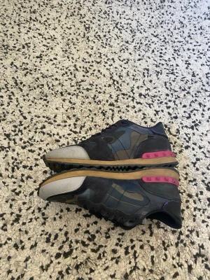 Blå camo sneakers med rosa detaljer - Snygga sneakers med blått camo-mönster, grå tå och coola rosa detaljer på hälen. Skorna har en låg profil och en beige sula med svart yttersula. Perfekta för dig som vill sticka ut med din stil.