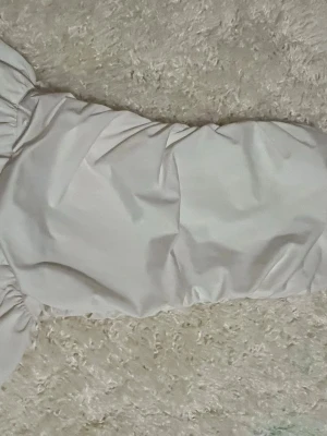 Vit offshoulder kortklänning - Trendig vit kortklänning med offshoulder-design och puffiga ärmar. Klänningen har en figurnära passform och är tillverkad i ett mjukt bomullsliknande material. Perfekt för dig som vill ha en stilren och modern look.