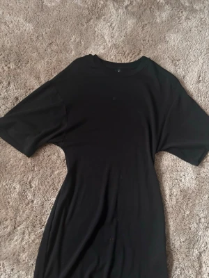 Svart t-shirtklänning Gina Tricot - En enkel svart t-shirtklänning från Gina Tricot i storlek M. Klänningen har rund halsringning, korta ärmar och rak passform. Perfekt basplagg att styla med sneakers eller boots. Passar S och M